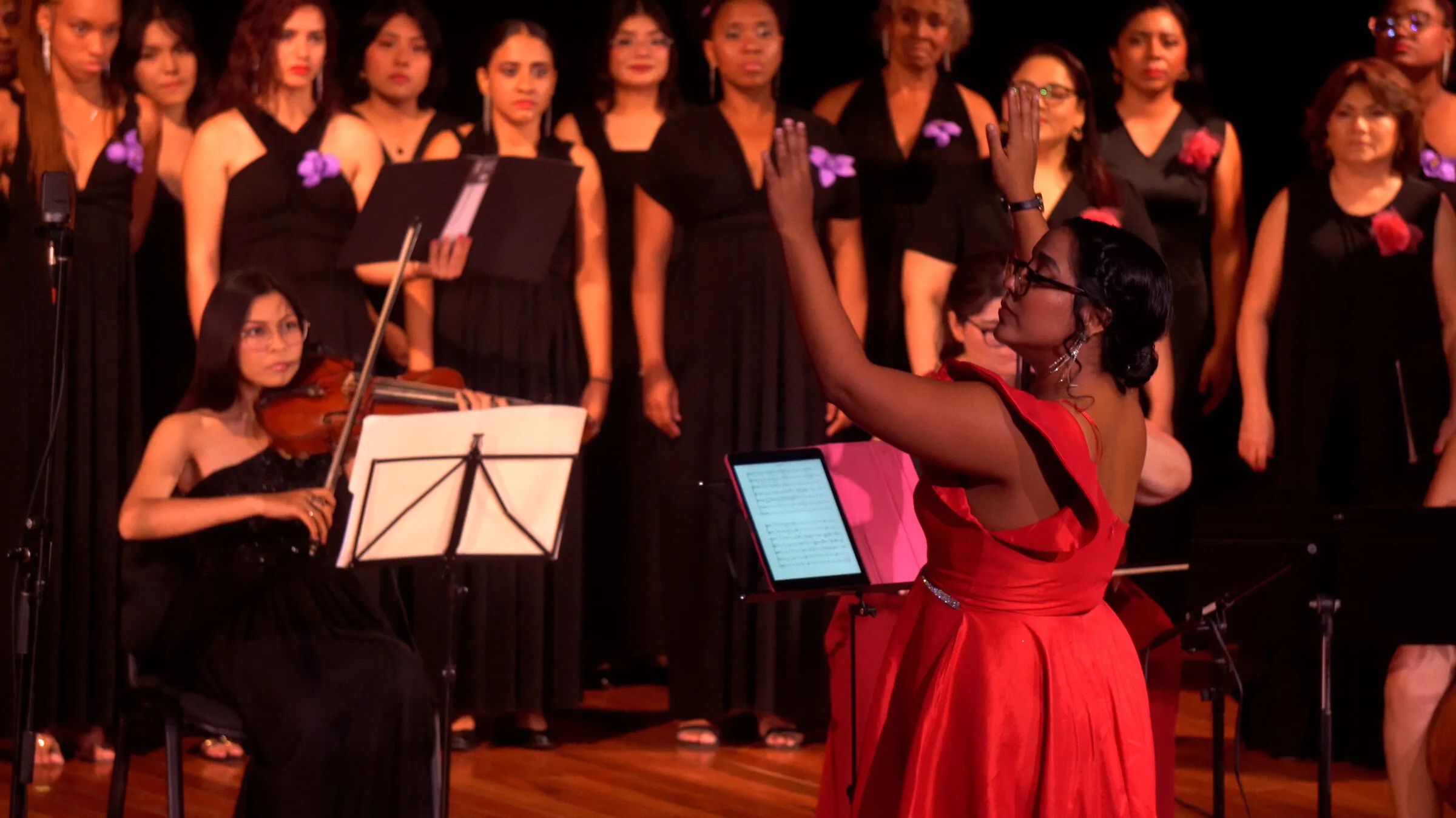 Blanca Fuentes, in red, conducts a women’s choir and a violinist